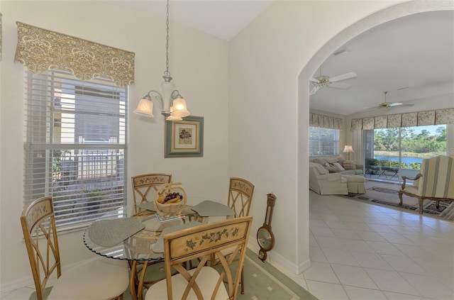 dining room featuring light tile patterned floors, baseboards, lofted ceiling, arched walkways, and ceiling fan with notable chandelier