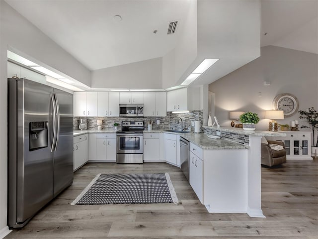 kitchen featuring stainless steel appliances, visible vents, a sink, vaulted ceiling with skylight, and a peninsula