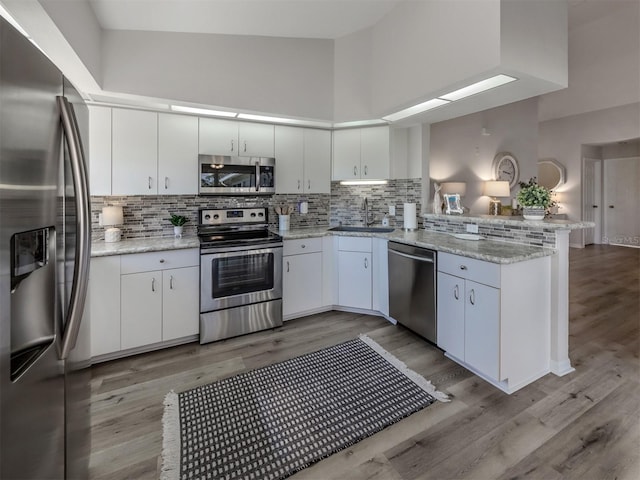 kitchen featuring tasteful backsplash, a peninsula, stainless steel appliances, white cabinetry, and a sink