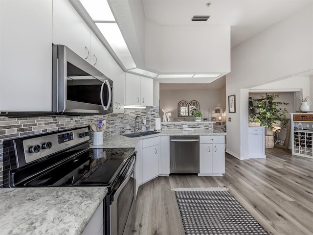 kitchen with stainless steel appliances, a sink, white cabinetry, decorative backsplash, and light wood finished floors