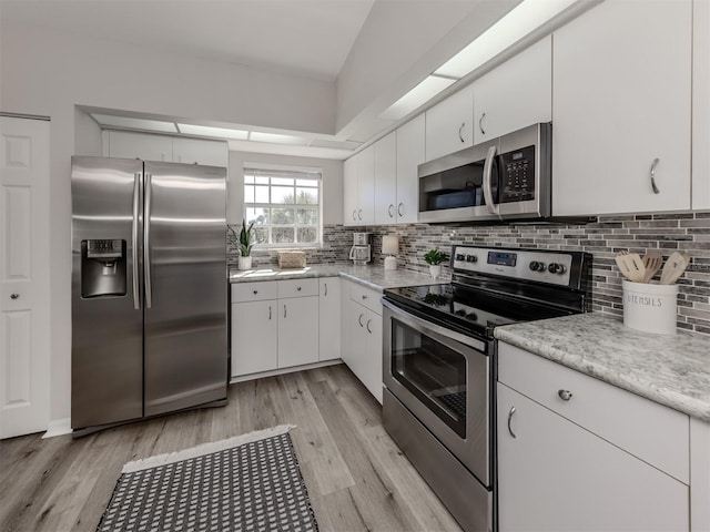 kitchen featuring stainless steel appliances, light countertops, light wood-style flooring, and decorative backsplash