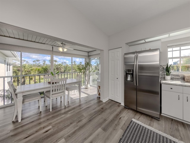 kitchen with lofted ceiling, light wood-style flooring, white cabinets, stainless steel fridge with ice dispenser, and tasteful backsplash