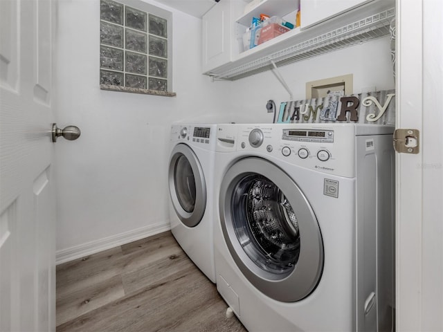 laundry area featuring light wood-type flooring, cabinet space, washer and clothes dryer, and baseboards