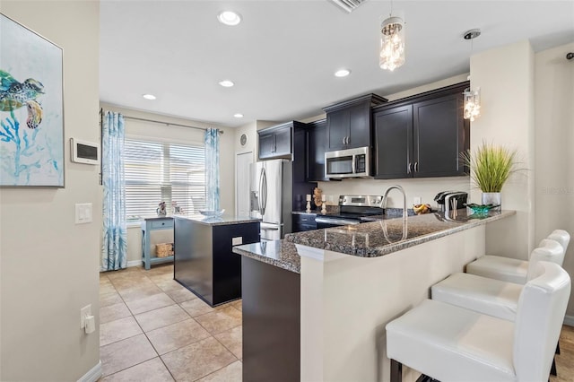 kitchen featuring dark stone counters, a breakfast bar, a center island, stainless steel appliances, and pendant lighting