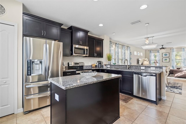 kitchen featuring appliances with stainless steel finishes, open floor plan, a center island, hanging light fixtures, and a sink