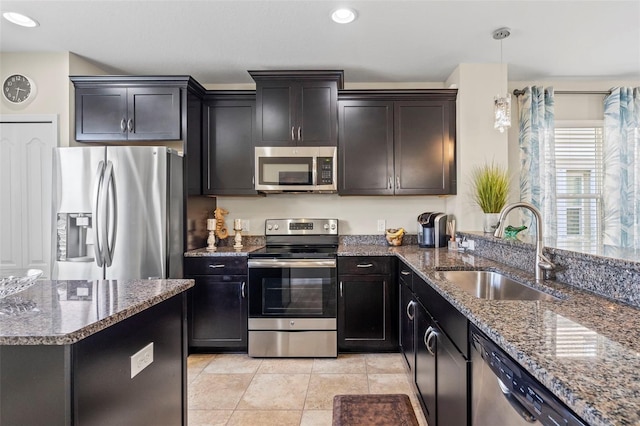 kitchen with light tile patterned floors, dark stone counters, appliances with stainless steel finishes, pendant lighting, and a sink