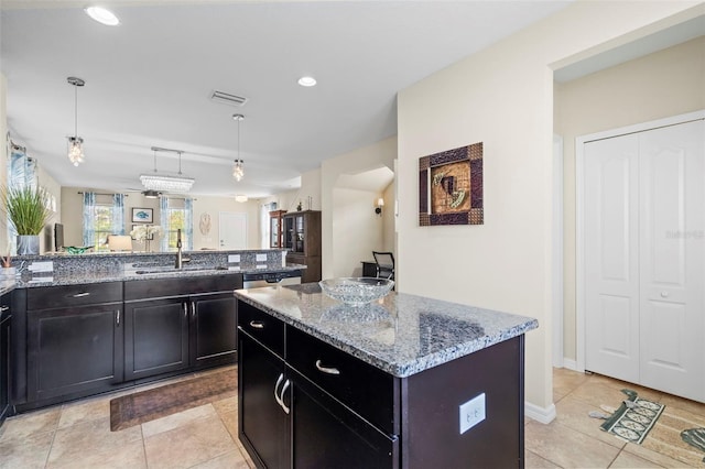 kitchen with visible vents, a kitchen island, light stone counters, decorative light fixtures, and a sink