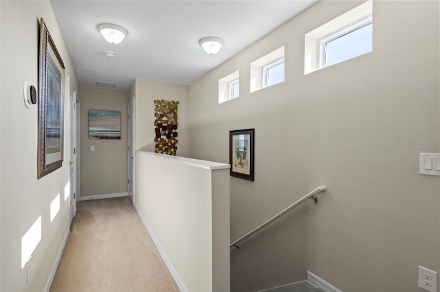 hallway with baseboards, light carpet, and an upstairs landing