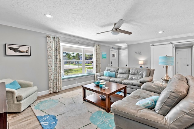 living area featuring a barn door, baseboards, a ceiling fan, crown molding, and light wood-style floors