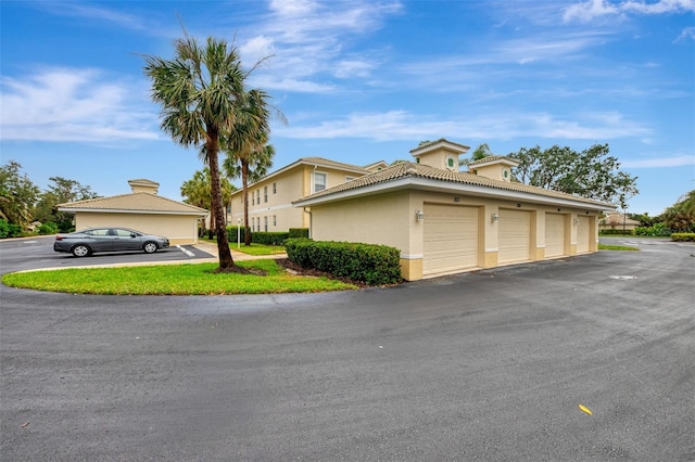 view of front of home with a tile roof, community garages, and stucco siding