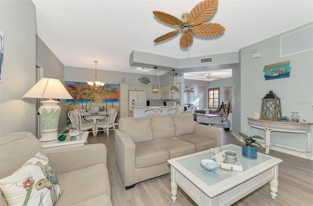 living area with baseboards, visible vents, light wood finished floors, and ceiling fan with notable chandelier