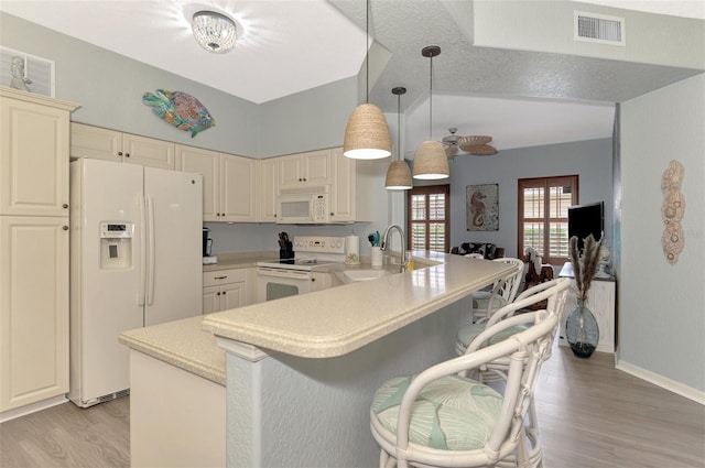 kitchen with light countertops, visible vents, a sink, white appliances, and a kitchen bar