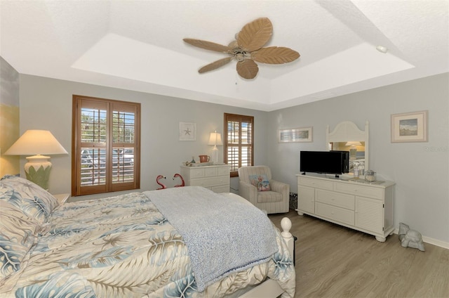 bedroom with ceiling fan, light wood-style flooring, baseboards, french doors, and a tray ceiling