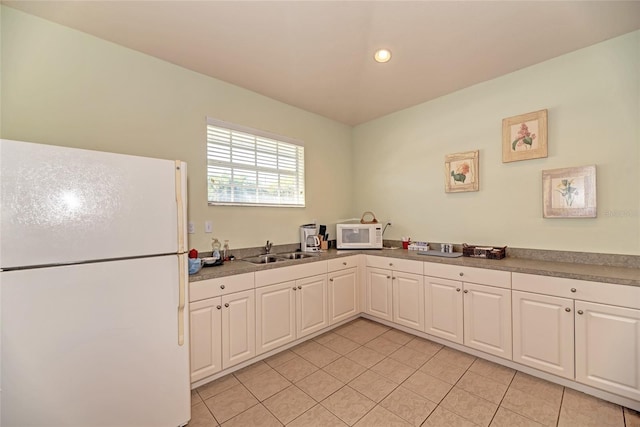 kitchen with light tile patterned floors, white appliances, a sink, and white cabinets