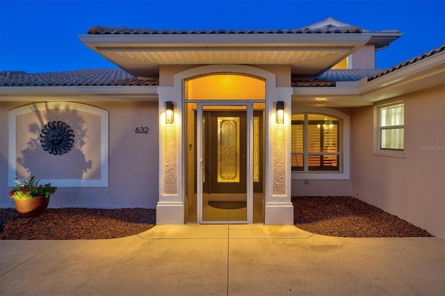 view of exterior entry with a tile roof and stucco siding