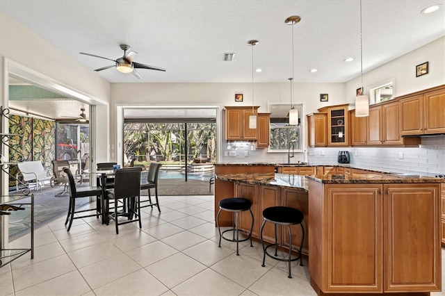 kitchen with visible vents, dark stone counters, a kitchen island, brown cabinets, and backsplash