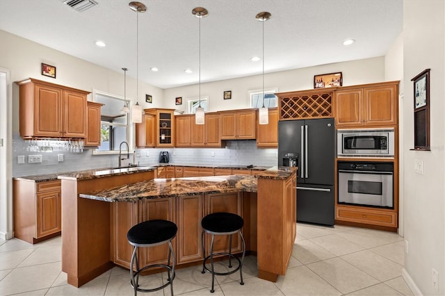 kitchen featuring appliances with stainless steel finishes, backsplash, a center island, dark stone counters, and brown cabinetry