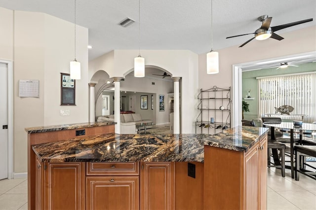 kitchen with arched walkways, brown cabinets, decorative columns, and light tile patterned floors