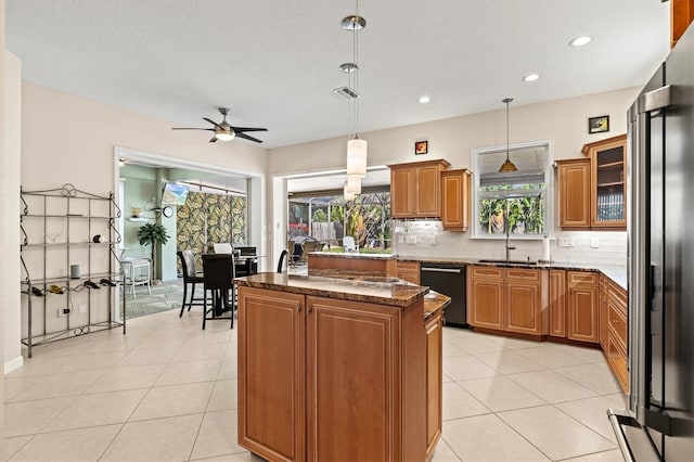 kitchen with tasteful backsplash, black dishwasher, dark stone counters, a kitchen island, and high quality fridge