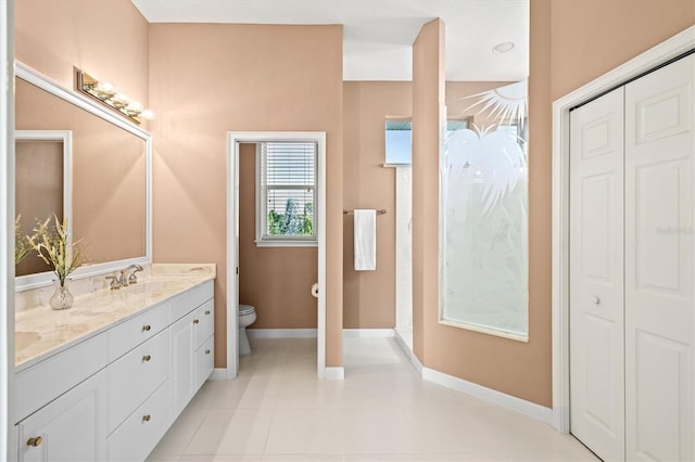 bathroom featuring tile patterned flooring, toilet, a sink, baseboards, and double vanity