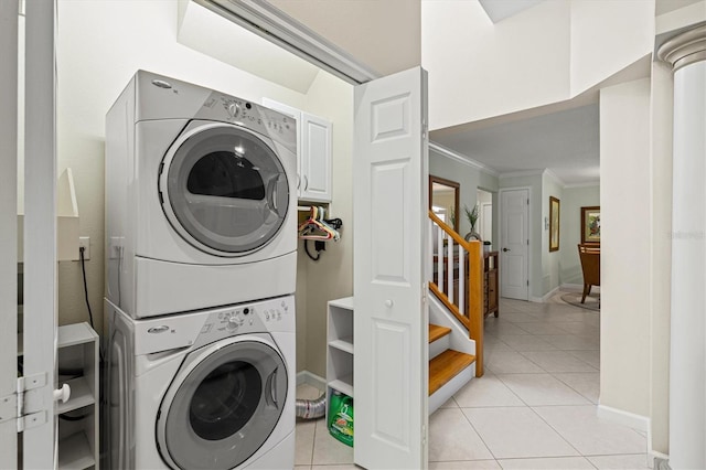 clothes washing area featuring light tile patterned floors, stacked washer and dryer, ornamental molding, laundry area, and baseboards