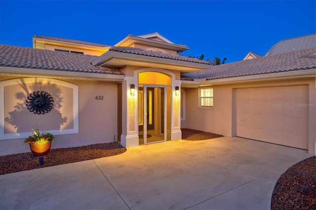 view of front of house with a garage, driveway, a tiled roof, and stucco siding