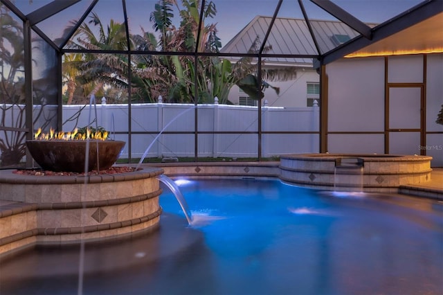 pool with an outdoor fire pit, glass enclosure, fence, and a hot tub