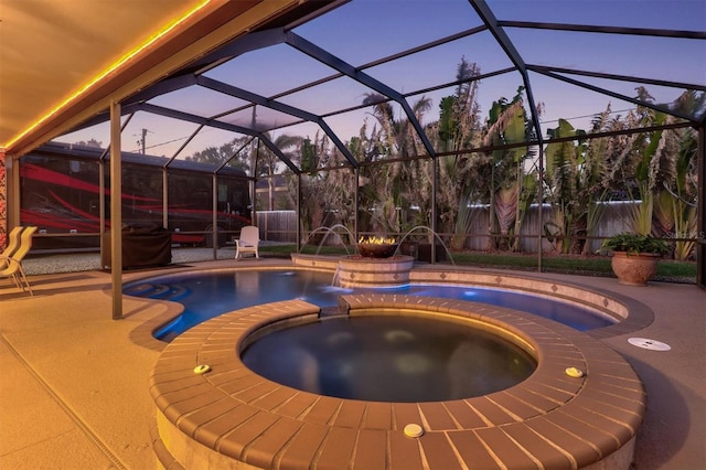 pool at dusk with a pool with connected hot tub, a lanai, a patio area, and fence