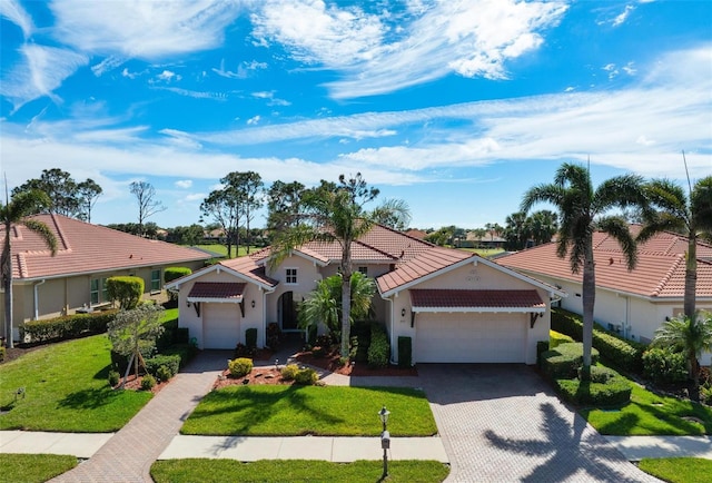 mediterranean / spanish home featuring an attached garage, a tile roof, decorative driveway, stucco siding, and a front yard