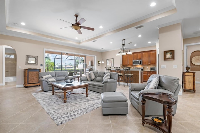 living area with light tile patterned floors, visible vents, a raised ceiling, arched walkways, and crown molding