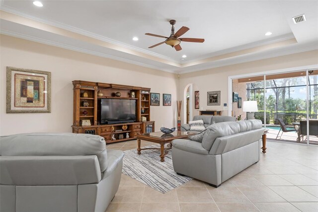 living area featuring arched walkways, light tile patterned floors, visible vents, ornamental molding, and a tray ceiling