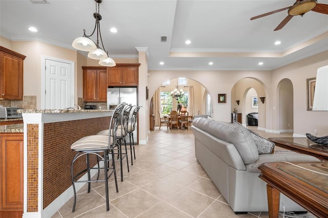 living area featuring arched walkways, light tile patterned floors, a raised ceiling, and recessed lighting