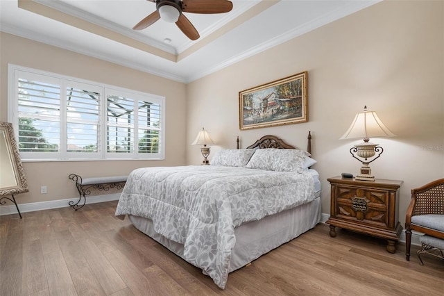 bedroom with ornamental molding, light wood-type flooring, a raised ceiling, and baseboards