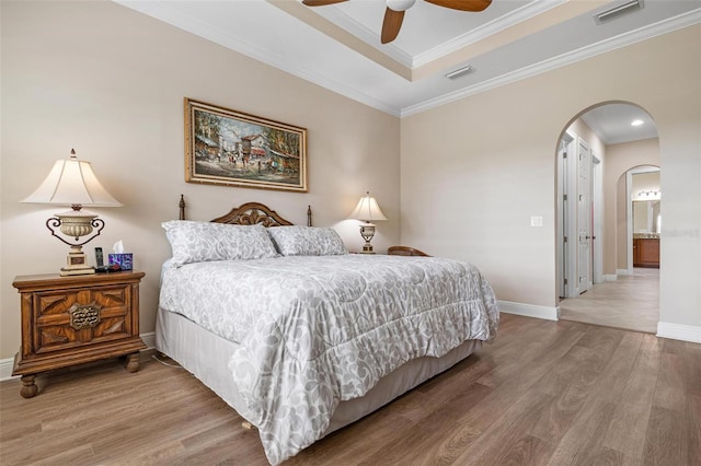 bedroom featuring arched walkways, wood finished floors, visible vents, baseboards, and crown molding