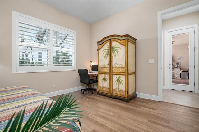 bedroom featuring light wood-type flooring, built in study area, and baseboards