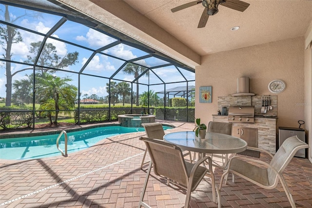 view of patio featuring a pool with connected hot tub, an outdoor kitchen, area for grilling, a ceiling fan, and glass enclosure