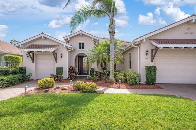 view of front of house featuring a front yard, decorative driveway, an attached garage, and stucco siding