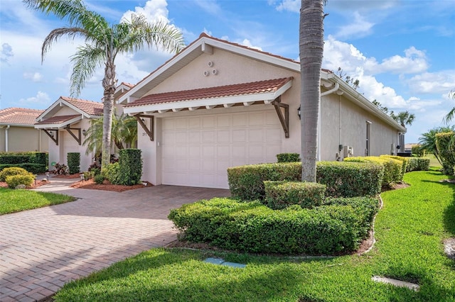 view of front facade with a garage, a tiled roof, decorative driveway, a front lawn, and stucco siding