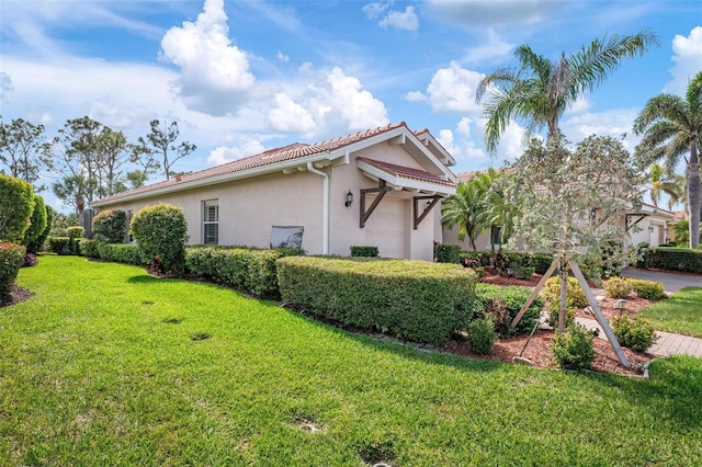 view of property exterior with an attached garage, a tile roof, a lawn, and stucco siding