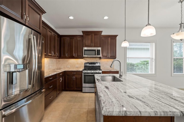 kitchen featuring appliances with stainless steel finishes, a sink, a kitchen island with sink, and pendant lighting