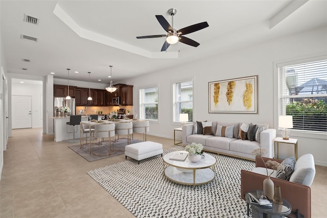 living area with a ceiling fan, a tray ceiling, visible vents, and baseboards