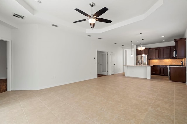 unfurnished living room featuring visible vents, baseboards, ceiling fan, a tray ceiling, and light tile patterned flooring