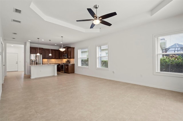 unfurnished living room featuring a tray ceiling, visible vents, ceiling fan, and baseboards