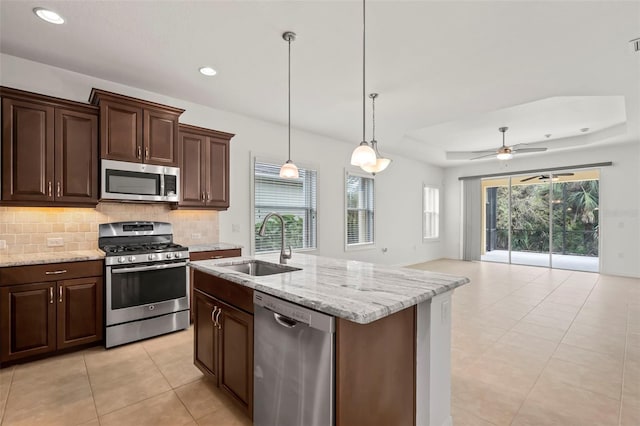 kitchen with a tray ceiling, stainless steel appliances, hanging light fixtures, open floor plan, and a sink