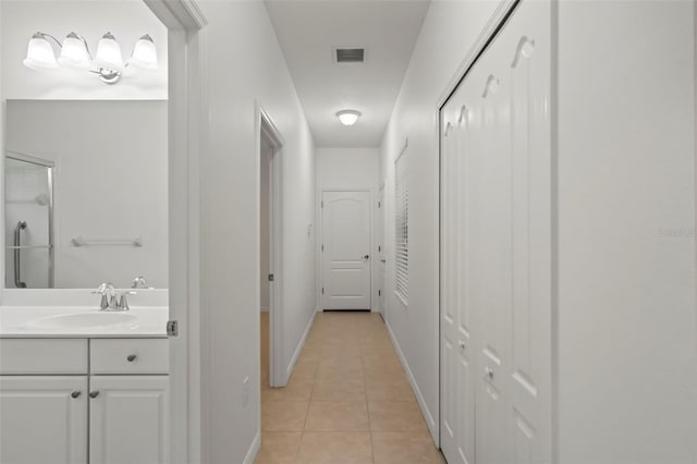 corridor featuring visible vents, a sink, baseboards, and light tile patterned floors