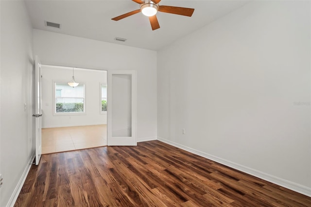 empty room with dark wood-type flooring, a ceiling fan, visible vents, and baseboards