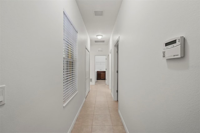 hallway with baseboards, visible vents, and light tile patterned flooring