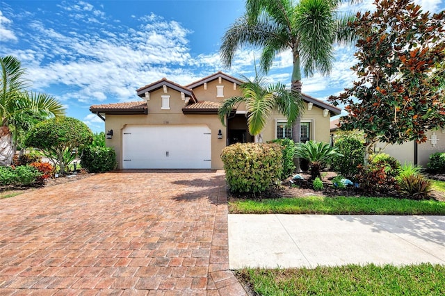 mediterranean / spanish house featuring a tiled roof, decorative driveway, an attached garage, and stucco siding