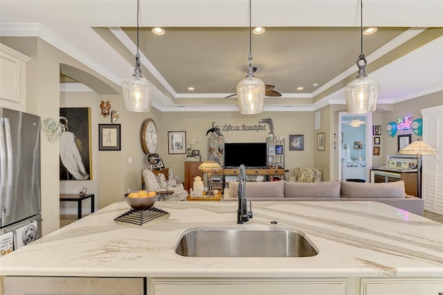 kitchen with light stone counters, open floor plan, freestanding refrigerator, a kitchen island with sink, and a sink