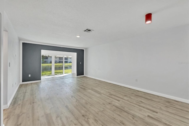 empty room featuring baseboards, a textured ceiling, visible vents, and light wood-style floors